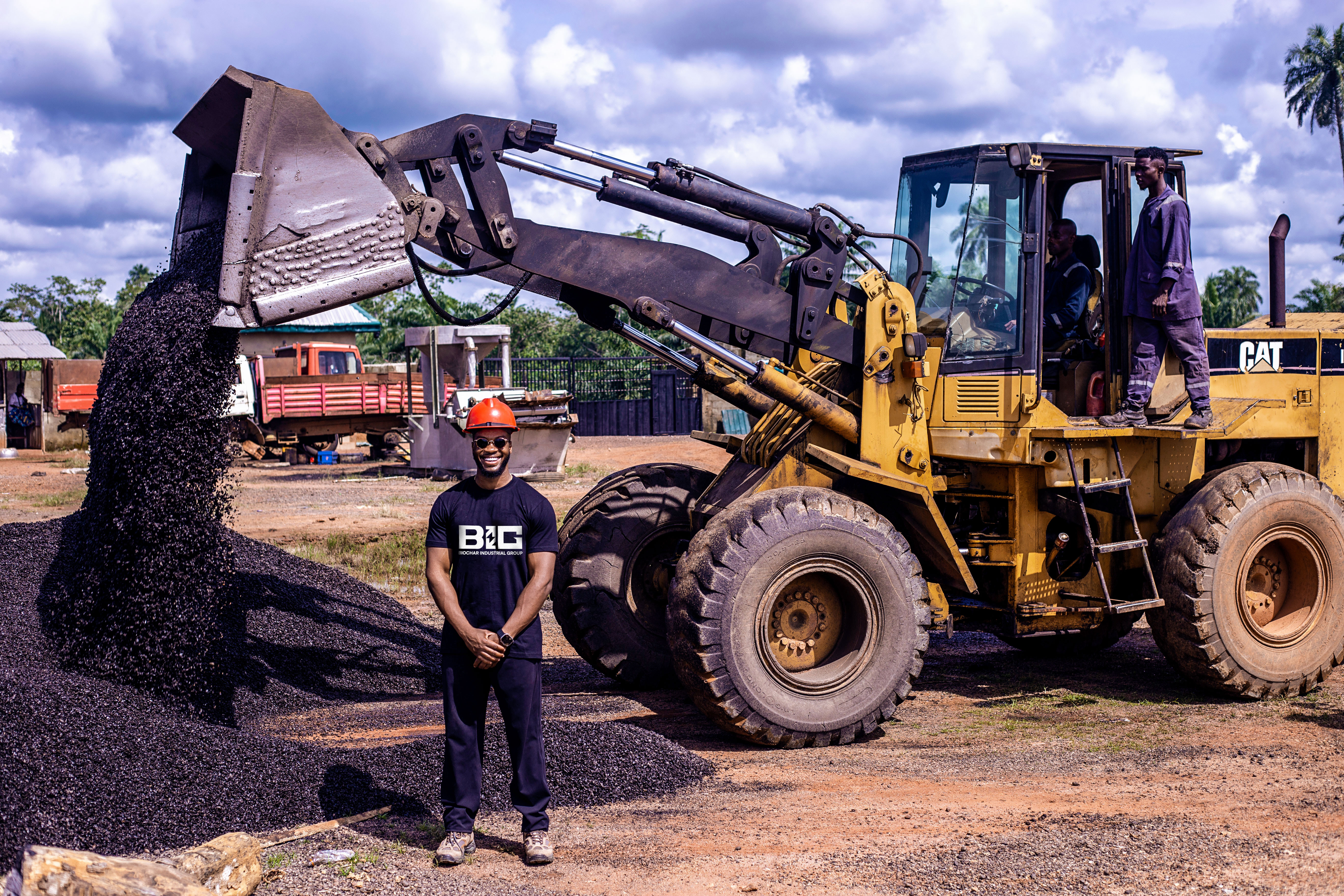 A wheel loader tipping fresh biochar beside a member of the Biochar Industrial Group team at a processing site in Nigeria.
